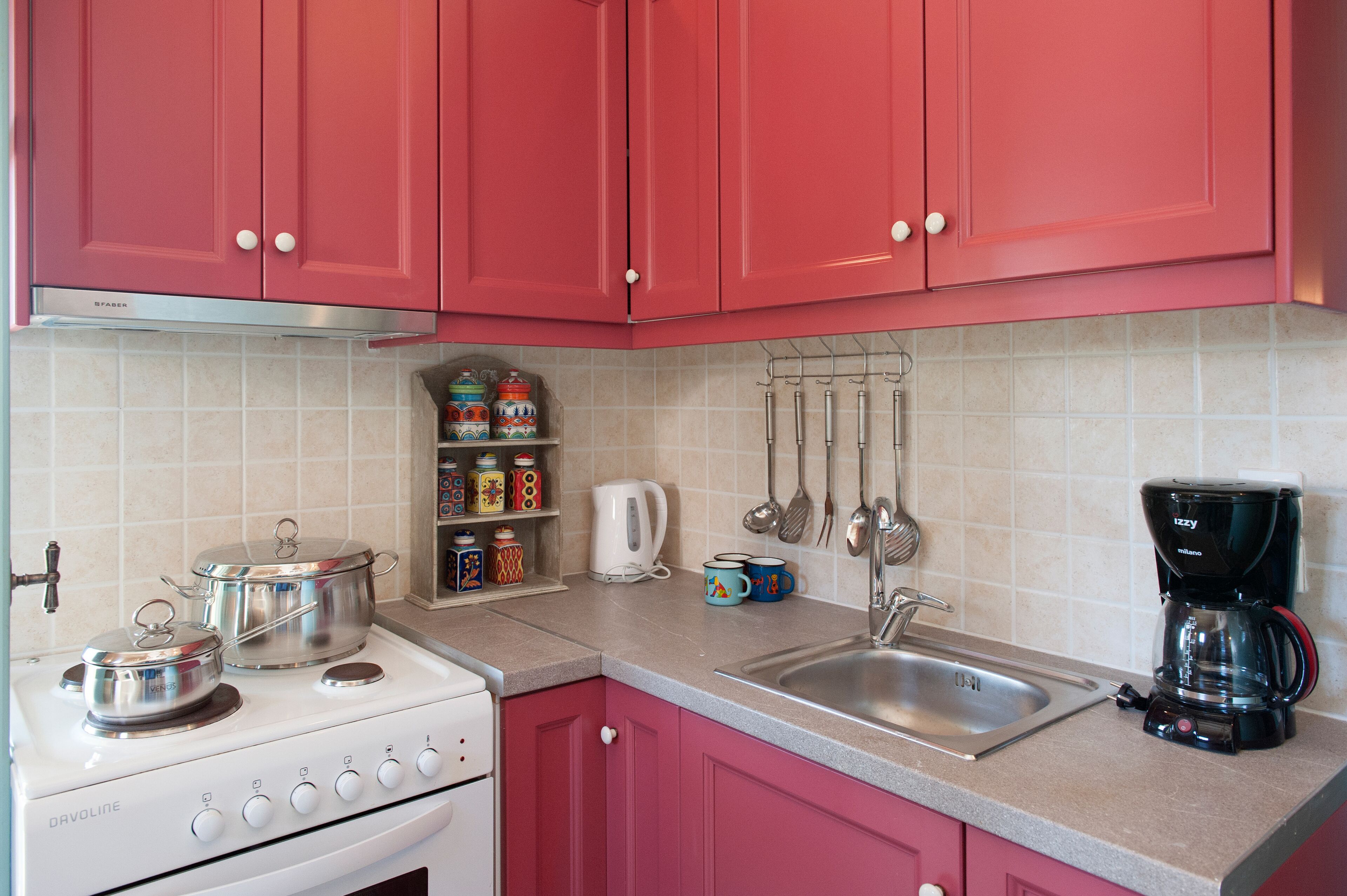 Una cocina con armarios rosados, una estufa blanca, una cafetera y diversos utensilios de cocina.