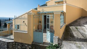 Un bâtiment jaune avec une porte et une grille bleues, des marches en pierre et des plantes en pot.