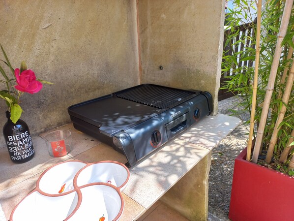 A barbecue grill with a control panel, a bottle of beer, a glass, and a pink flower on a stone ledge.
