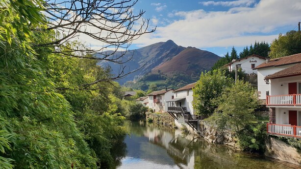 Ein Flussdorf mit traditionellen Häusern, einer Brücke und einem Berg im Hintergrund.
