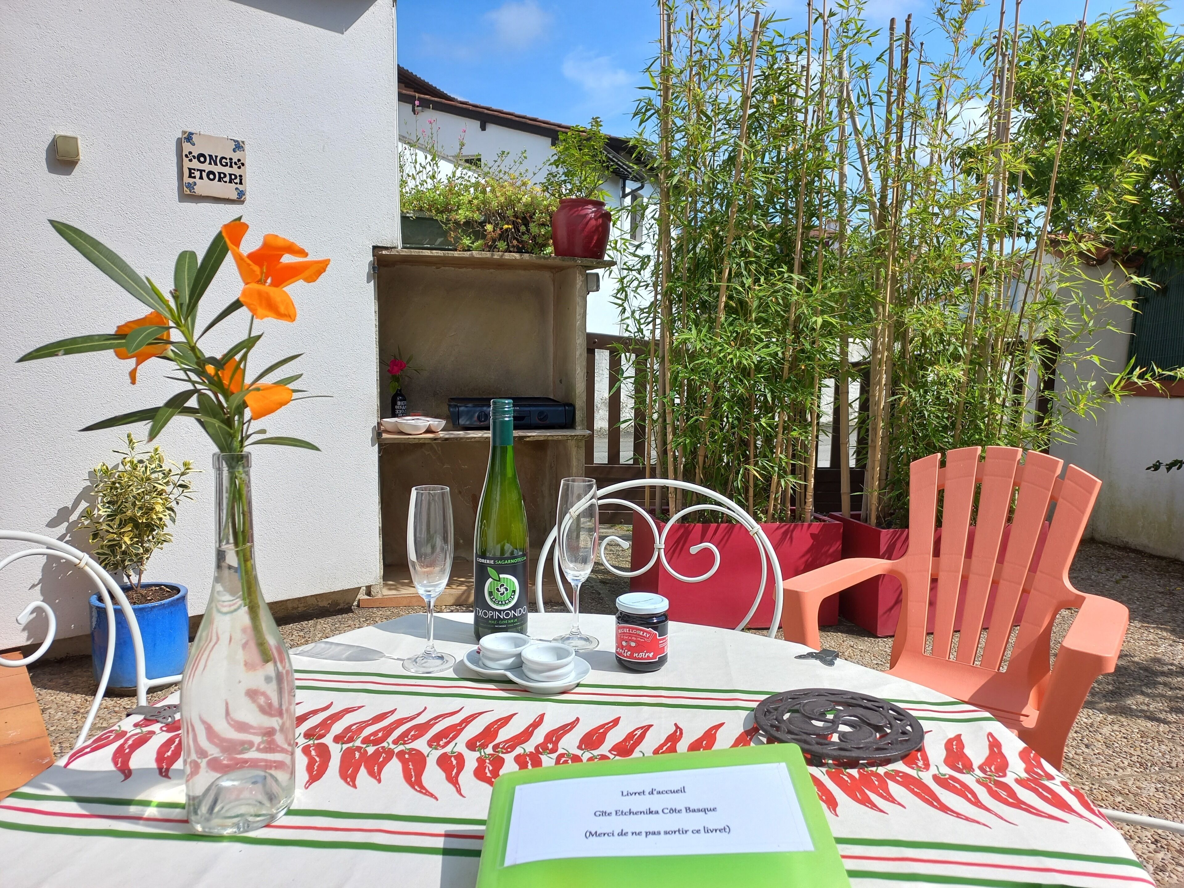 Een terras met een eettafel gedekt voor twee personen, een fles wijn, een potje jam en een menukaart.