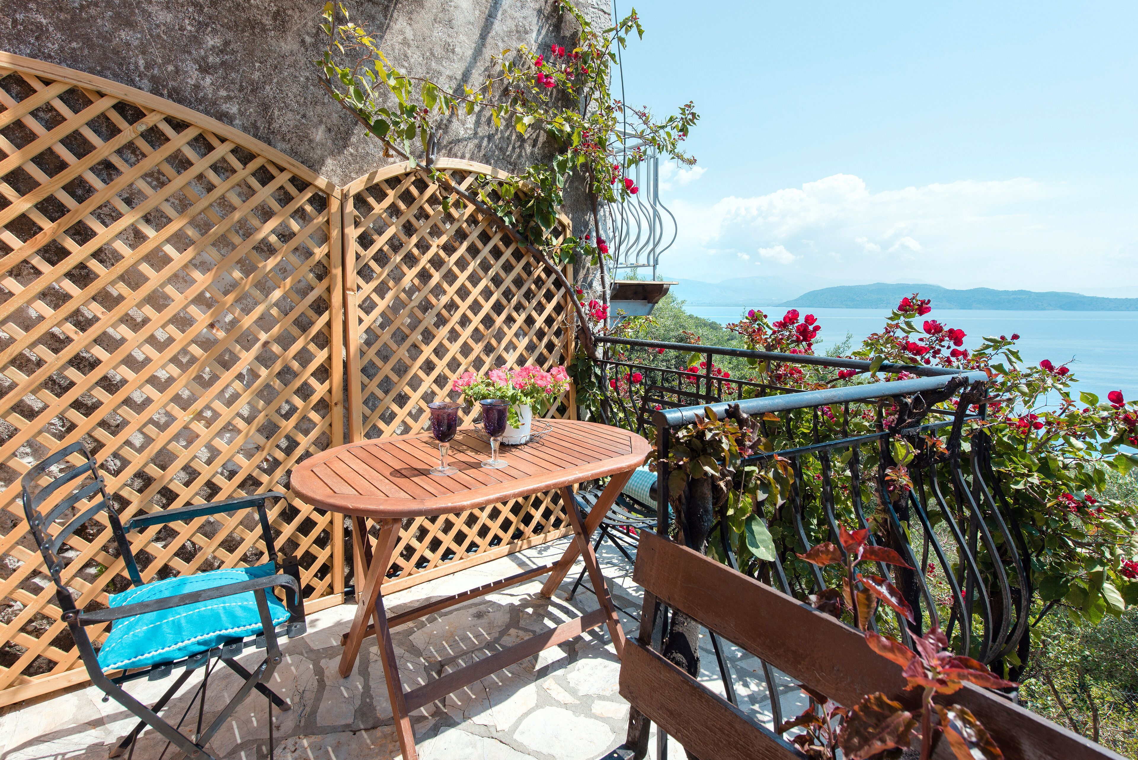 A wooden table and chairs on a balcony with a view of the sea.