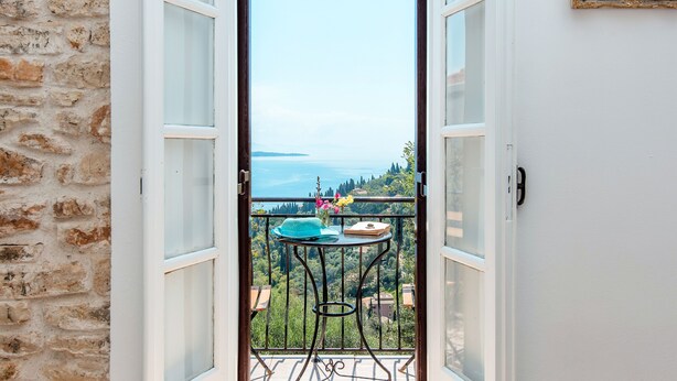 An open door leading to a balcony with a table, a hat, and flowers. - Nausica House (Corfu)