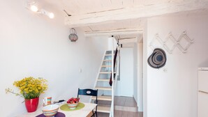 A kitchen with a white marble countertop, a red pot with yellow flowers, striped cups, and a bowl of fruit. A wooden ladder leads to a lofted area. - Nausica House (Corfu)