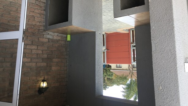 Una habitación con pared de ladrillo, techo de madera y ventana con vistas a edificios y árboles.