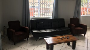 Una sala de estar con un sofá de cuero negro, dos sillones y una mesa de centro de madera.