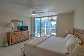Ein Schlafzimmer mit einem Bett, einem Fernseher auf einer Holzkommode, einem Deckenventilator und einem Balkon mit einem Sessel.