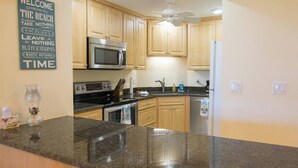 A kitchen with wooden cabinets, a granite countertop, a microwave, an oven, and a ceiling fan. - Charming Coastal Living: Gulf Views Await (Naples)