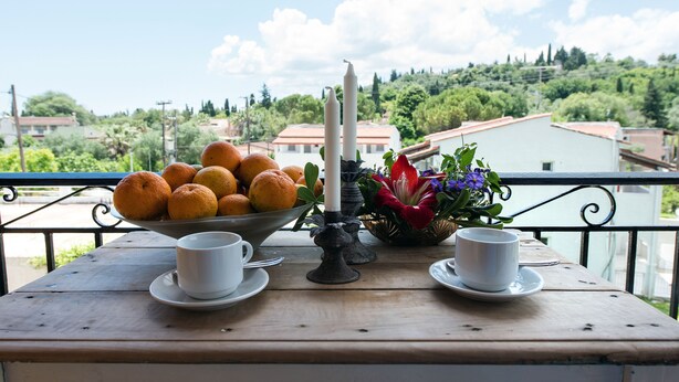 A table with a bowl of oranges, two white cups, a candle, and a flower arrangement. - Lydia Apartment (Corfu)
