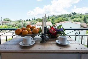 A table with a bowl of oranges, two white cups, a candle, and a flower arrangement. - Lydia Apartment (Corfu)