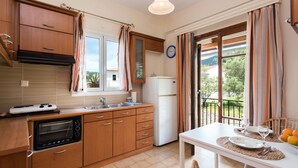 A kitchen with wooden cabinets, a built-in oven, a refrigerator, and a dining area with a table set for two. - Lydia Apartment (Corfu)