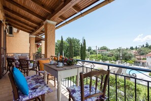 A balcony with wooden furniture, a table with a vase of flowers, and a view of the surrounding greenery and buildings.