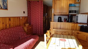 A cozy room with a wooden sofa, a dining table, and a kitchen area with wooden cabinets and appliances.