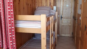 A wooden bunk bed room with a red curtain, a wooden wardrobe, and a door with a sign.