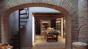 A narrow passageway with a brick archway leading to a dining area with a wooden table and chairs, a staircase, and a display of wine bottles. - Villa Fé with swimming pool in Assisi (Assisi)