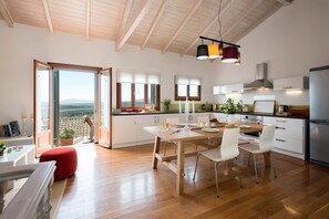 A spacious kitchen with wooden floors, a dining area with a table and chairs, and a view through large windows. - Lavender Cottage (Corfu)