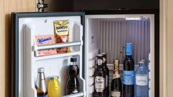 Un réfrigérateur ouvert contenant divers aliments et boissons, notamment une boîte de chocolats Hammer, un paquet de bonbons Haribo Goldbären et plusieurs bouteilles de bière et d’eau.