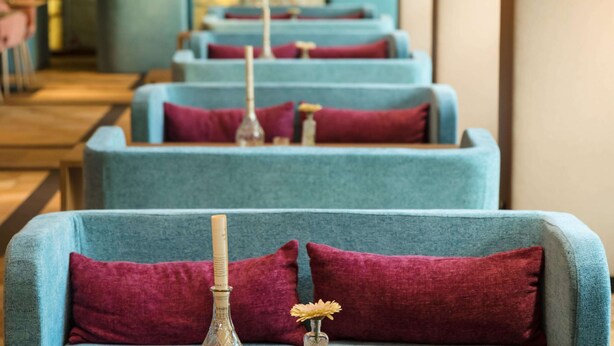 A row of blue armchairs with red cushions, a bottle, and a small vase with a flower. - Austria Trend Hotel Maximilian (Vienna)