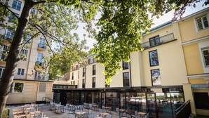An outdoor patio with tables and chairs, surrounded by buildings with balconies and windows. - Austria Trend Hotel Maximilian (Vienna)