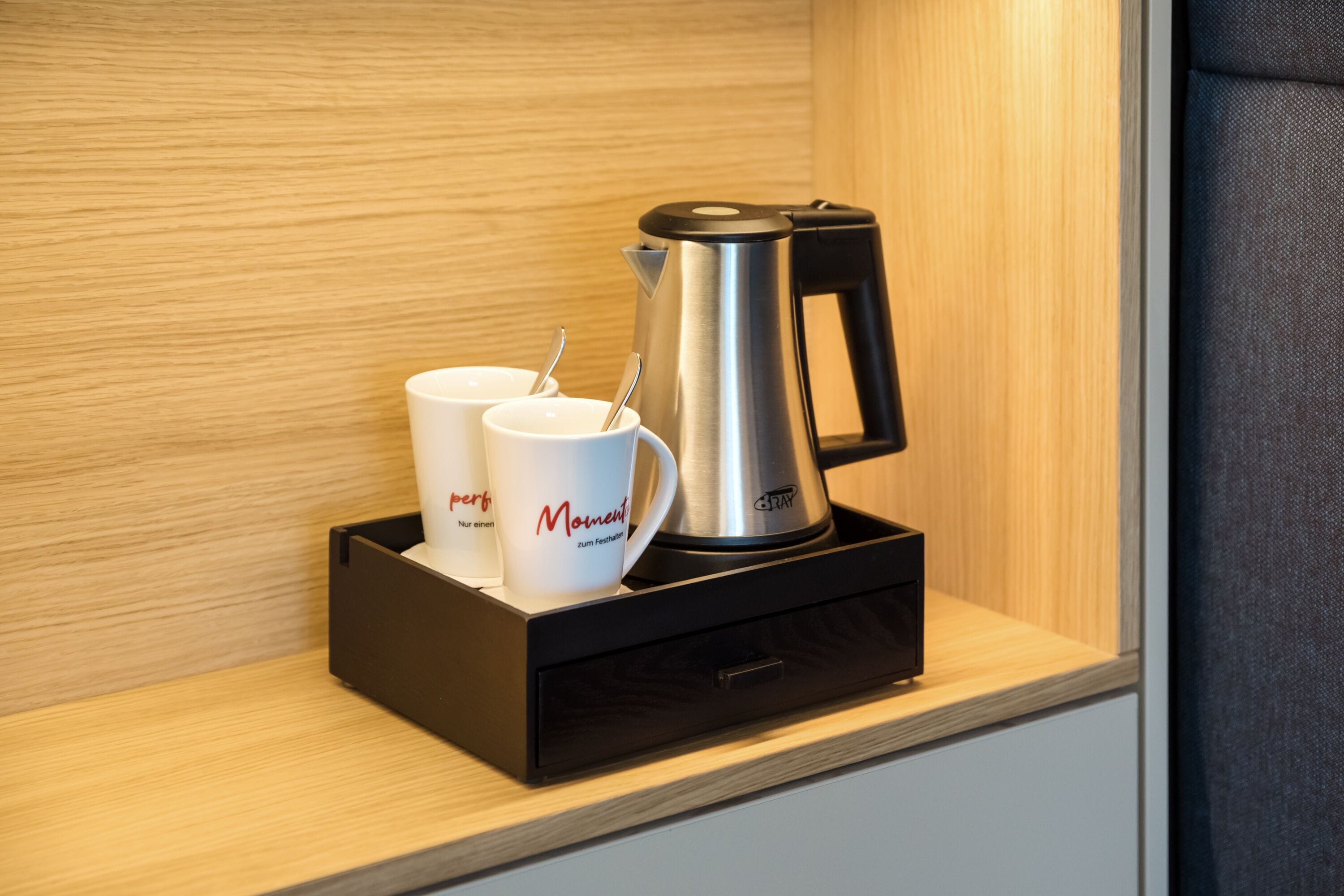 A coffee maker with two white cups on a wooden shelf.