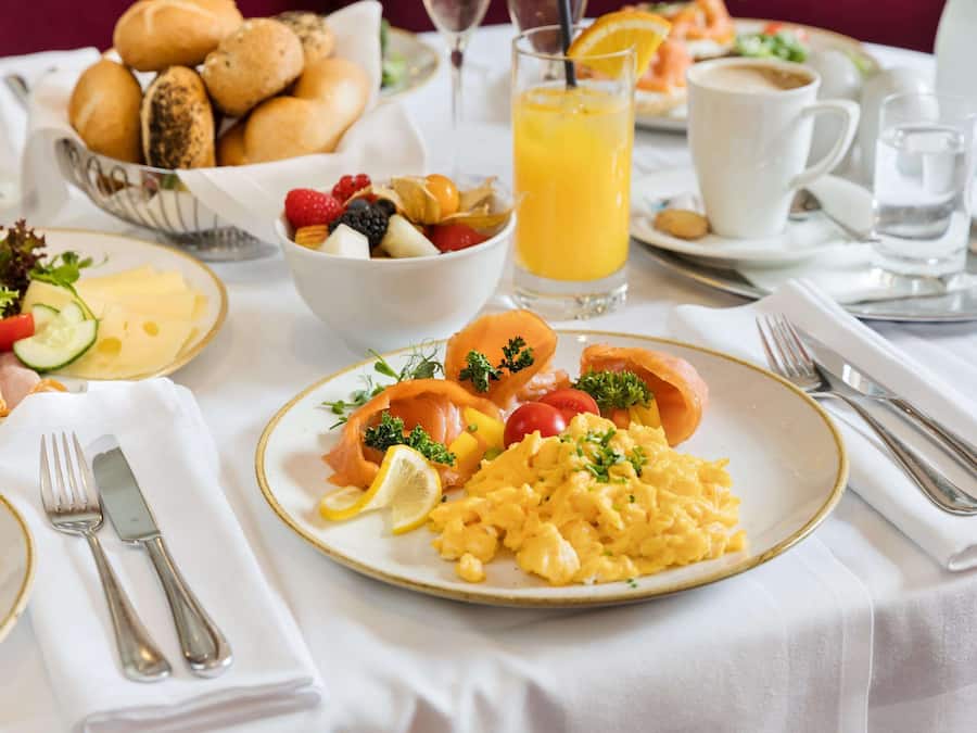 Un desayuno con huevos revueltos, salmón ahumado y un cuenco de fruta.