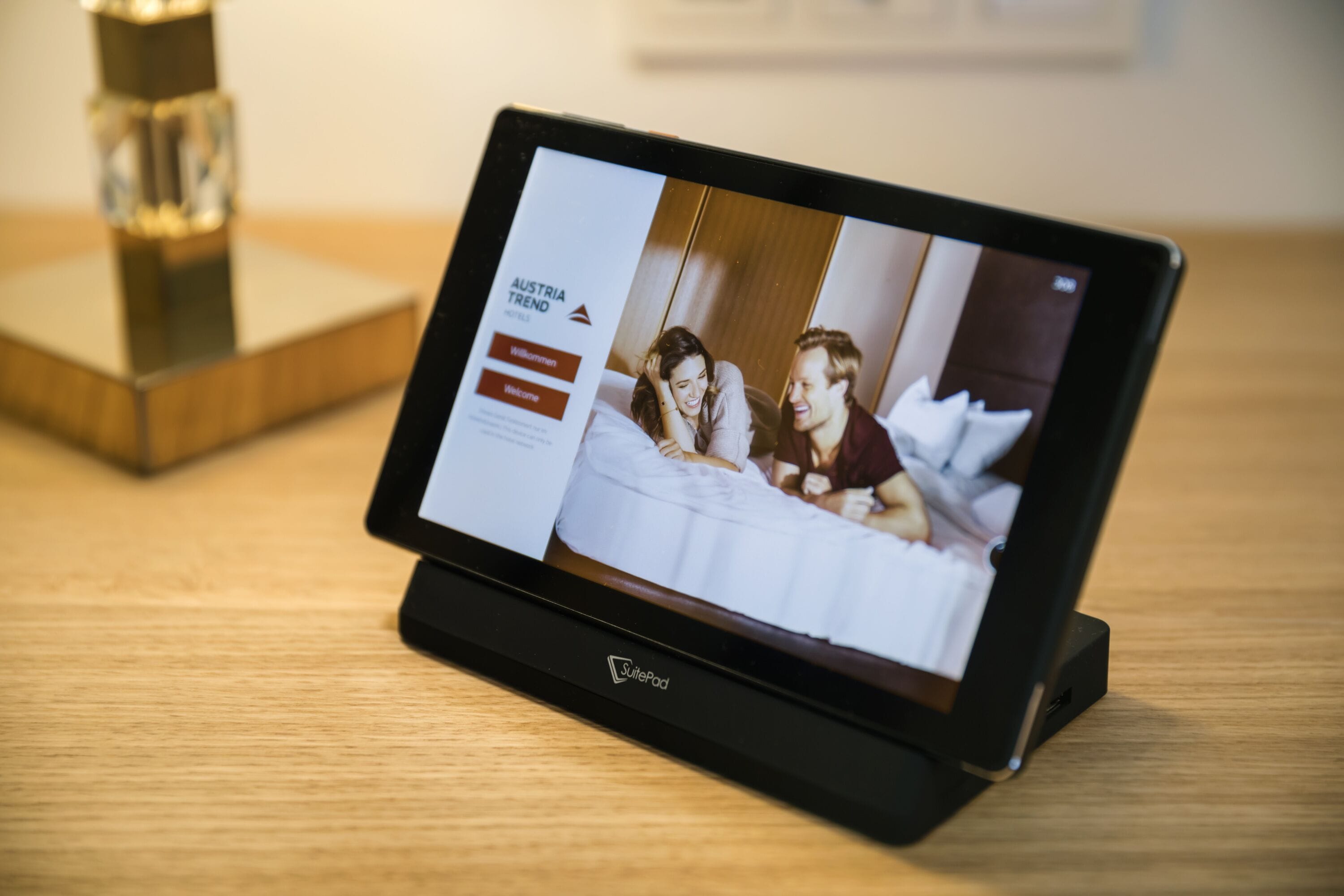Una tableta mostrando una habitación de hotel con una cama, una mesita de noche y un objeto decorativo sobre una superficie de madera.