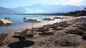 A beach with sun loungers and umbrellas, a clear sky, and mountains in the background. - Studio & large garden 200m Calvi beach (Calvi)
