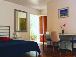 A bedroom with a bed, a desk, a chair, a mirror, and a door leading to a balcony. - Studio & large garden 200m Calvi beach (Calvi)