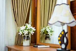 A wooden table with two glass vases of white flowers, a remote control, and a lamp with a unique design. - Van Long Green (Gia Van)