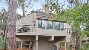 Une maison à deux étages avec un balcon, entourée d’arbres.