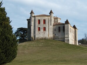 A historic stone building with multiple towers and red windows, situated on a grassy hill.