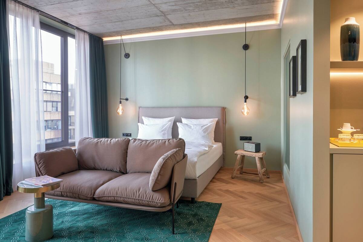 A modern hotel room with a bed, a sofa, a small table, and a desk.