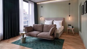 Una habitación de hotel moderna con sofá, cama y un pequeño taburete de madera.