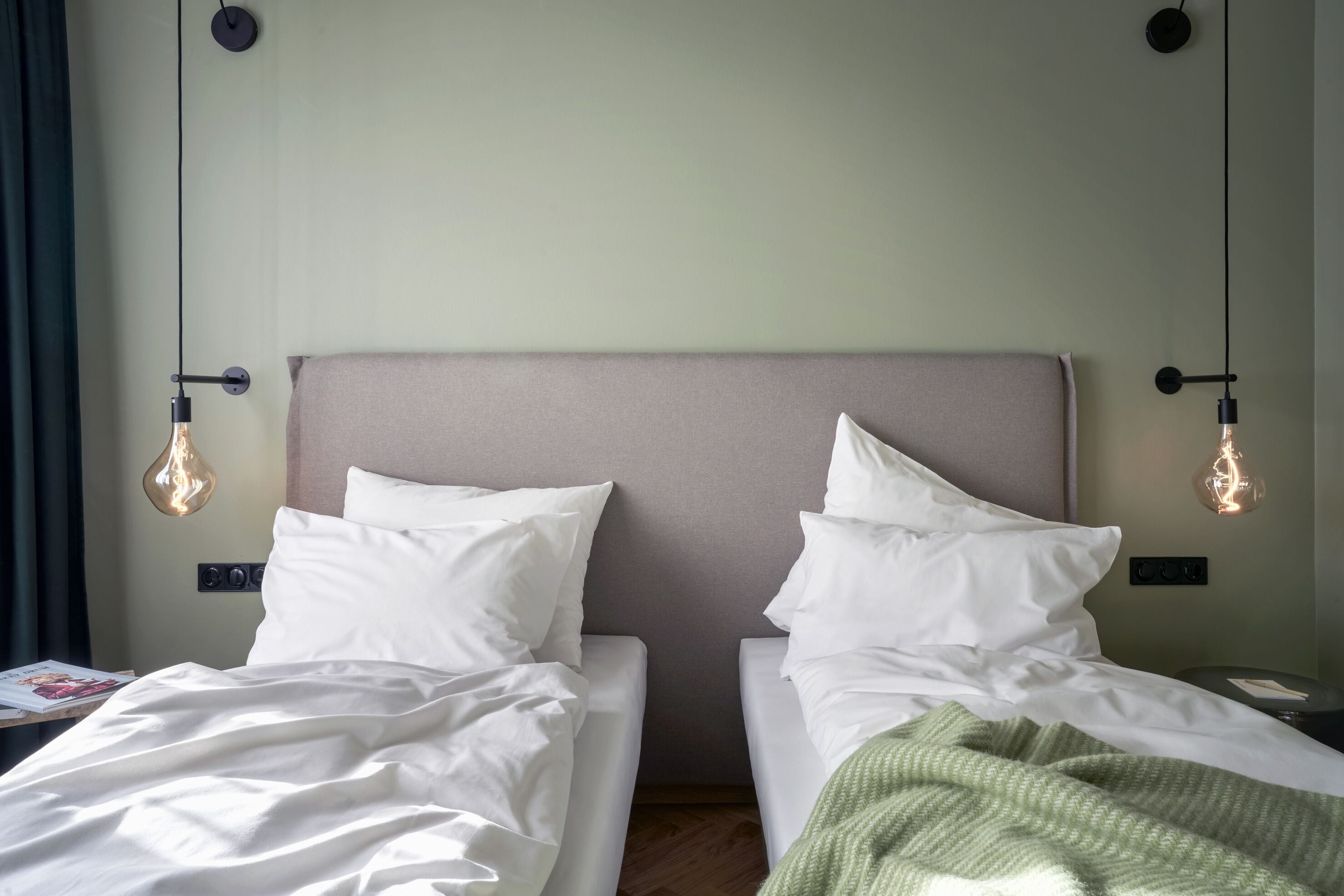A hotel room with two single beds, a neutral-colored headboard, and pendant lighting.