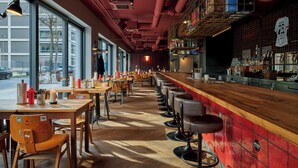 Un restaurante con mesas largas compartidas, taburetes de bar y un techo alto con conductos expuestos.