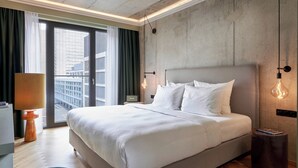 Una habitación de hotel moderna con una cama grande, vistas a la ciudad y una pared de detalles en concreto.
