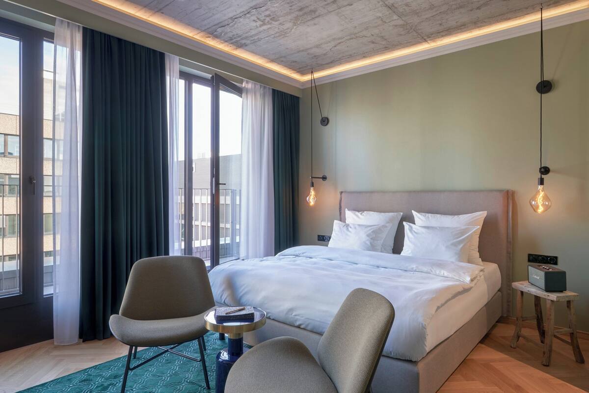 A hotel room with a large bed, two chairs, a small table, and a bedside table with a radio.