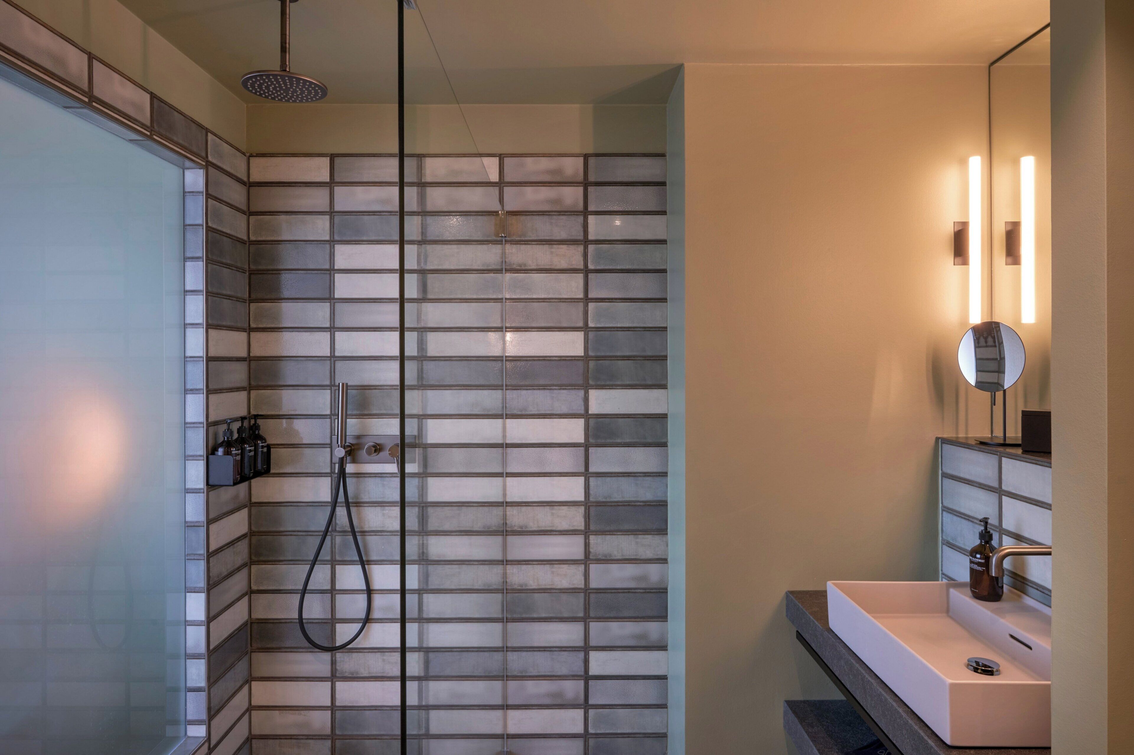 A modern bathroom with a glass shower enclosure, a white sink, and a mirror with integrated lighting.