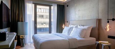 Une chambre d’hôtel moderne, dotée d’un grand lit, d’un bureau, d’une télévision et offrant une vue sur la ville par la fenêtre.