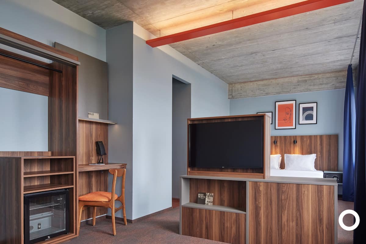 Ein kompakter, moderner Raum mit integriertem Holzmöbel, einem Flachbildfernseher und einem kleinen Kühlschrank.