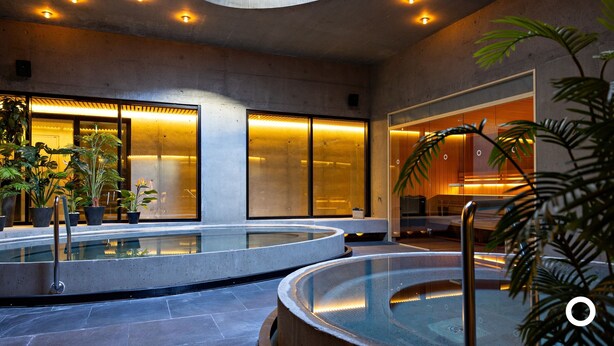 Un espace piscine intérieur moderne, doté de murs en verre et d’un éclairage chaleureux.
