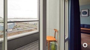 Een balkon met uitzicht op een parkeerplaats en gebouwen, met een stoel en een bank in de kamer.