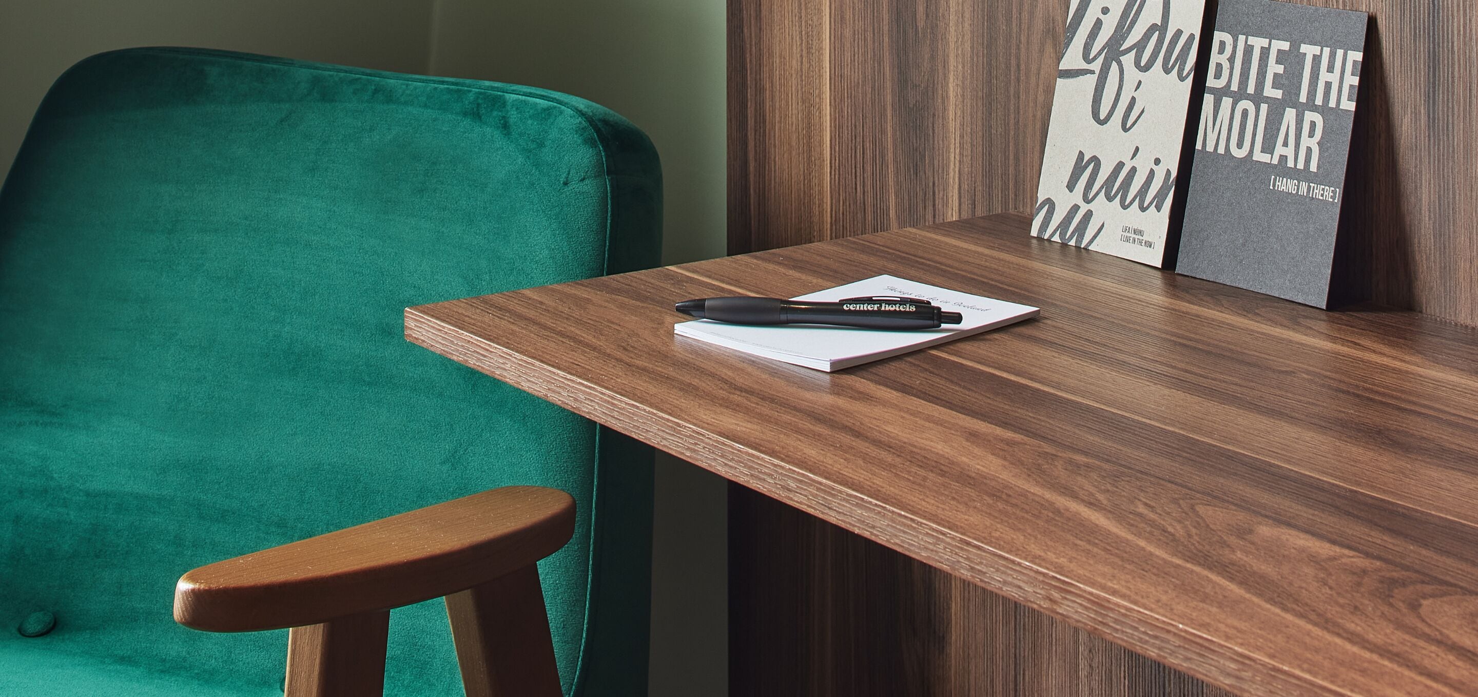 A wooden desk with a black pen and a notepad, a green chair, and two motivational posters on the wall.