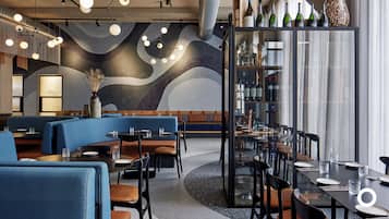 Un intérieur de restaurant moderne avec des sièges bleus, une cloison en verre et un présentoir à vin.