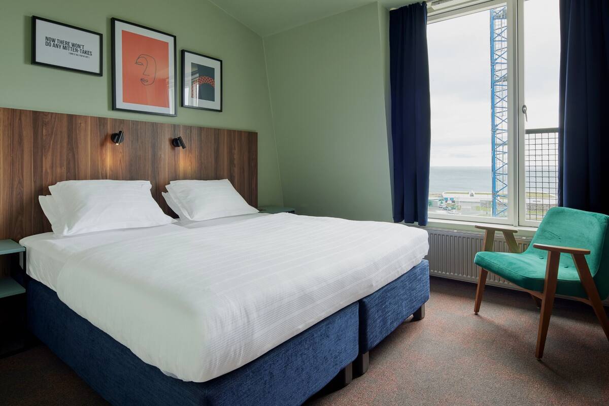 Ein Hotelzimmer mit einem großen Bett, einem Sessel und einem Fenster mit Blick auf eine Brücke.