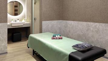 A room with a bed, a bench, a small table with towels, a mirror, and a sink.