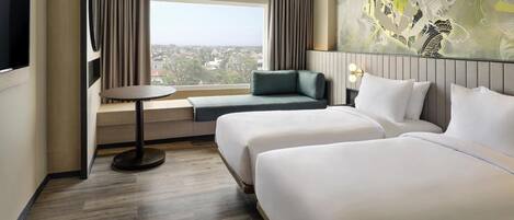 Habitación de hotel con dos camas, un sofá, una mesita y un ventanal grande con cortinas.