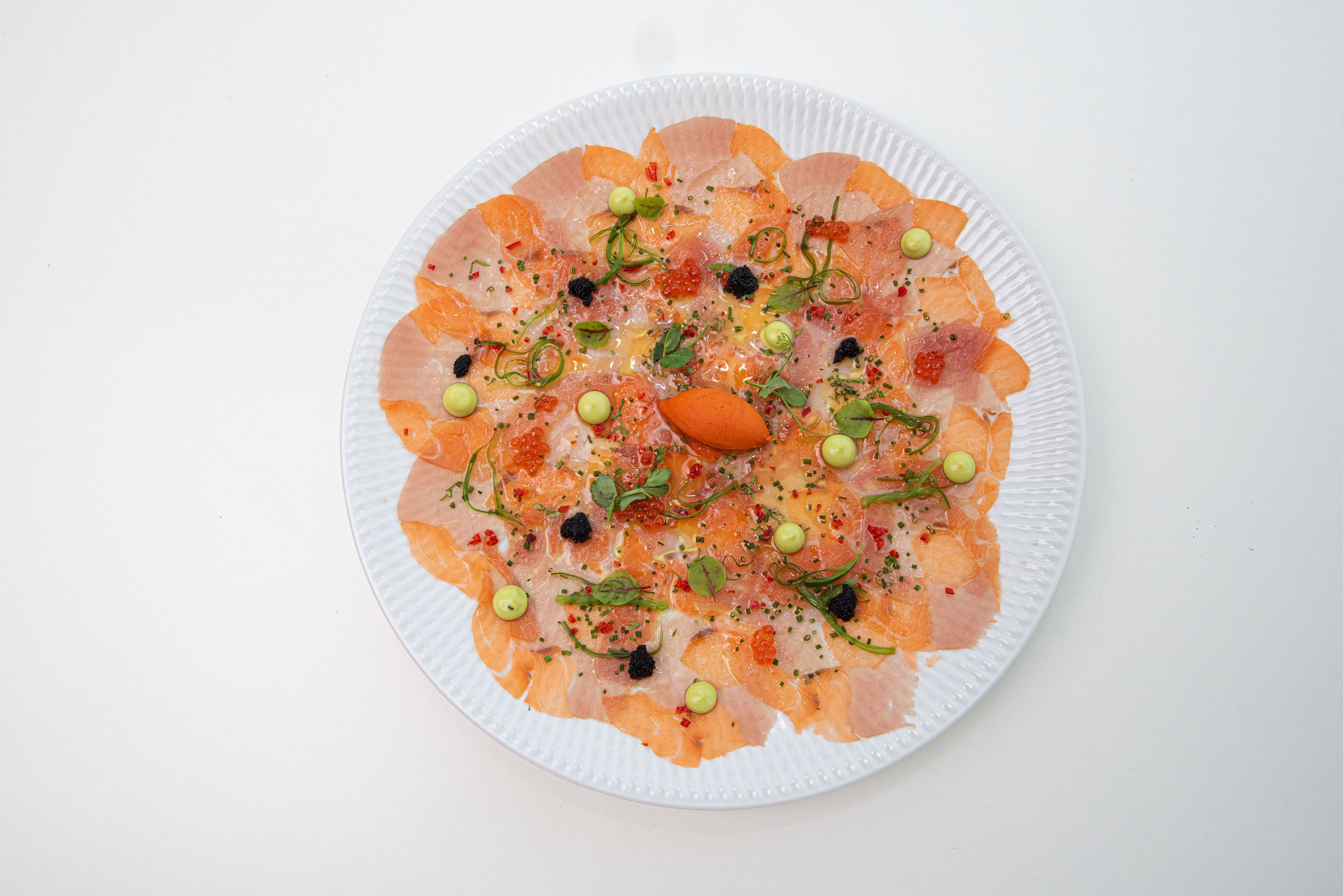 Un plato de papel con un guiso de mariscos, adornado con hierbas y pequeñas esferas verdes.
