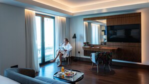 A modern hotel room with a large bed, a sitting area with a sofa, a dining table with breakfast, and a TV mounted on the wall. - Athens Capital Center Hotel-MGallery Collection (Athens)