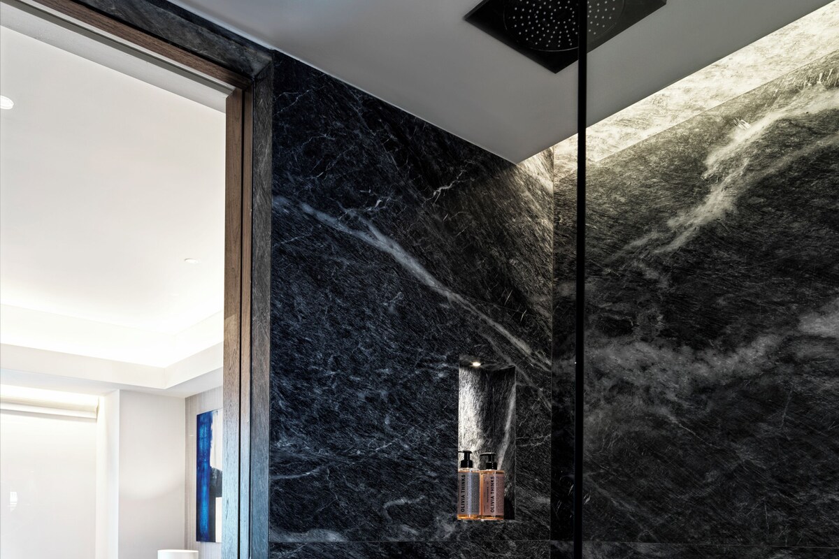 A modern bathroom with a marble wall, a shower, and a toilet.